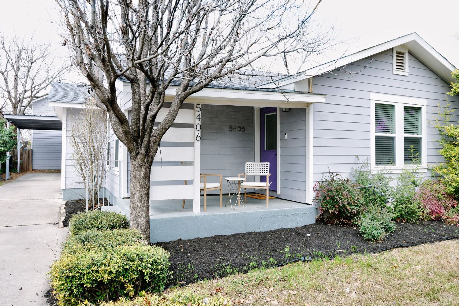 Side view of a light gray ranch-style house with white trim and mature landscaping in a residential neighborhood.