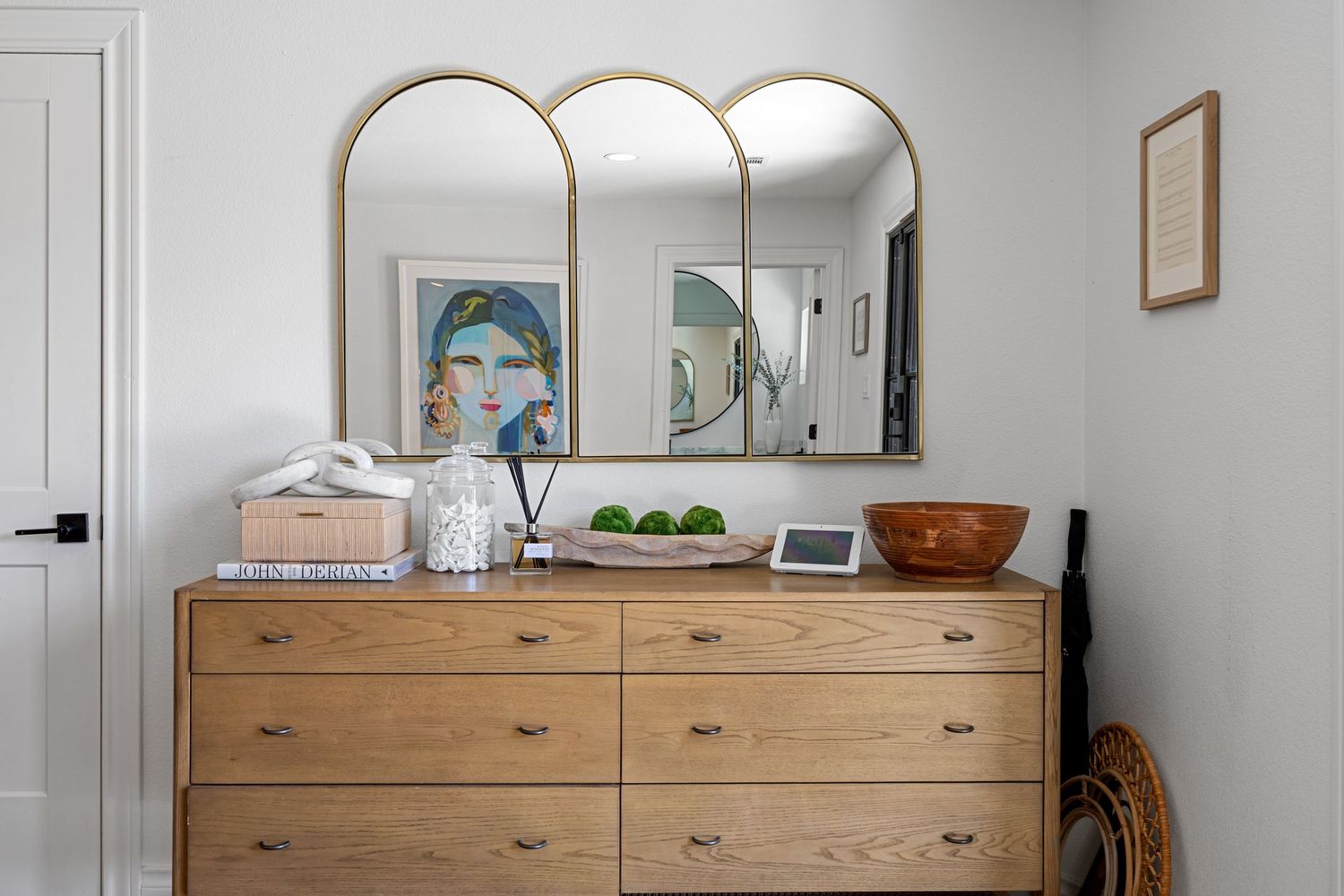 Stylish bedroom dresser with natural wood finish, tri-arch gold mirror, and decorative accents against a white wall.
