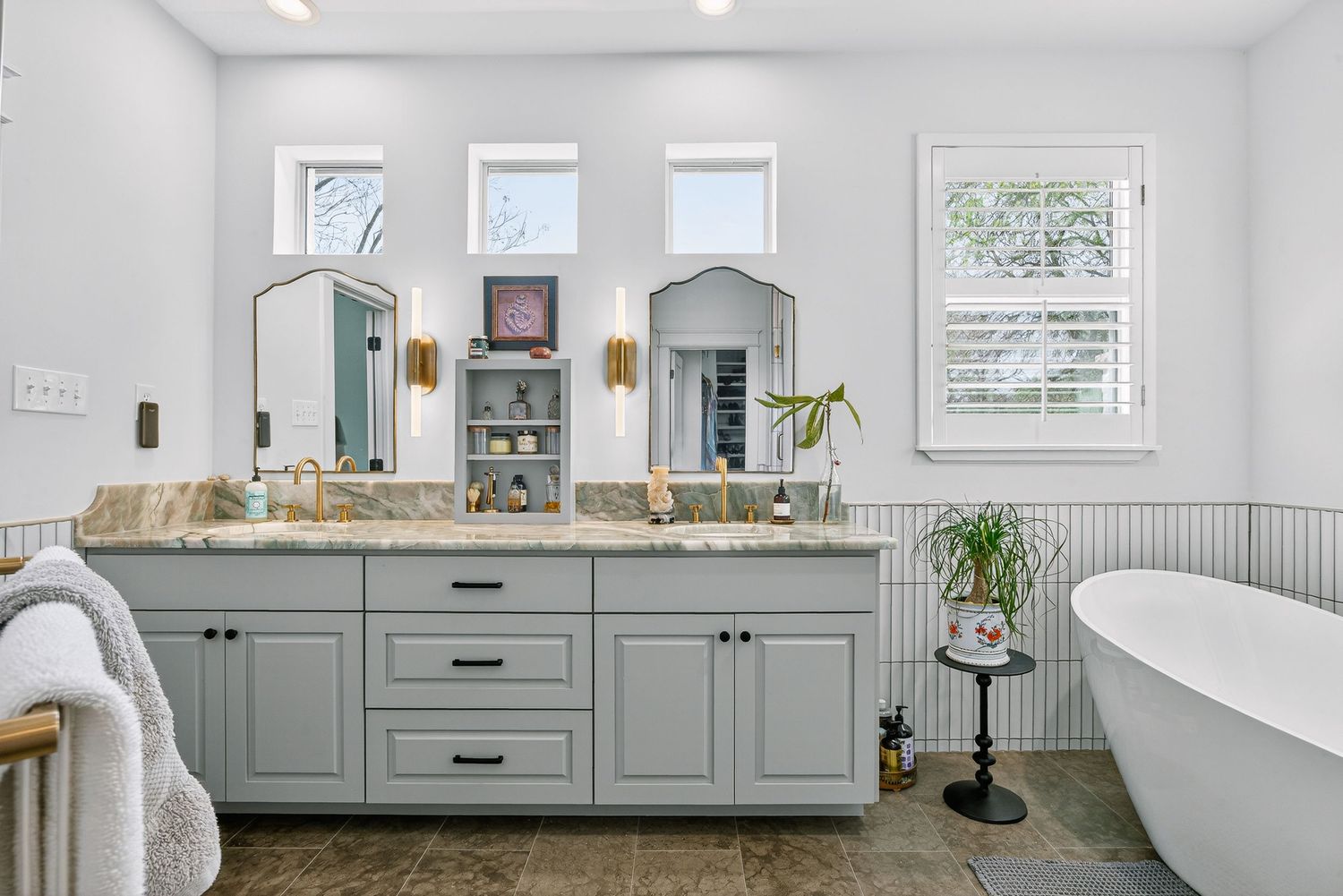 Elegant master bathroom with gray double vanity, granite countertops, arched mirrors, and a freestanding soaking tub.