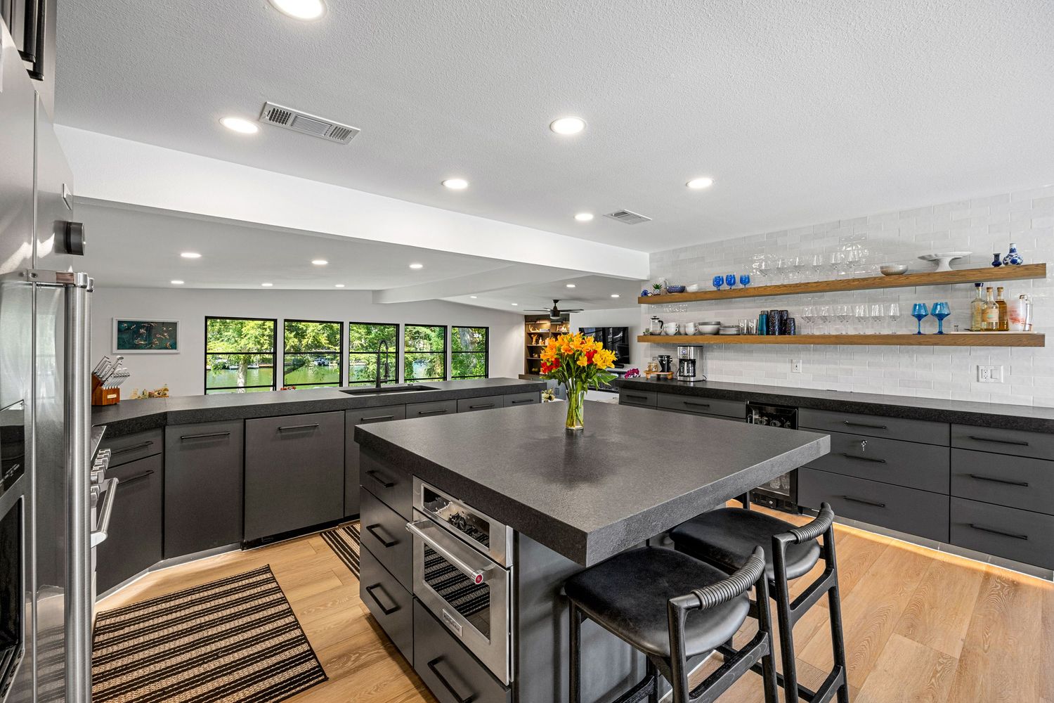 Sleek modern kitchen with dark gray cabinets, center island with wine storage, open shelving, and light hardwood floors.