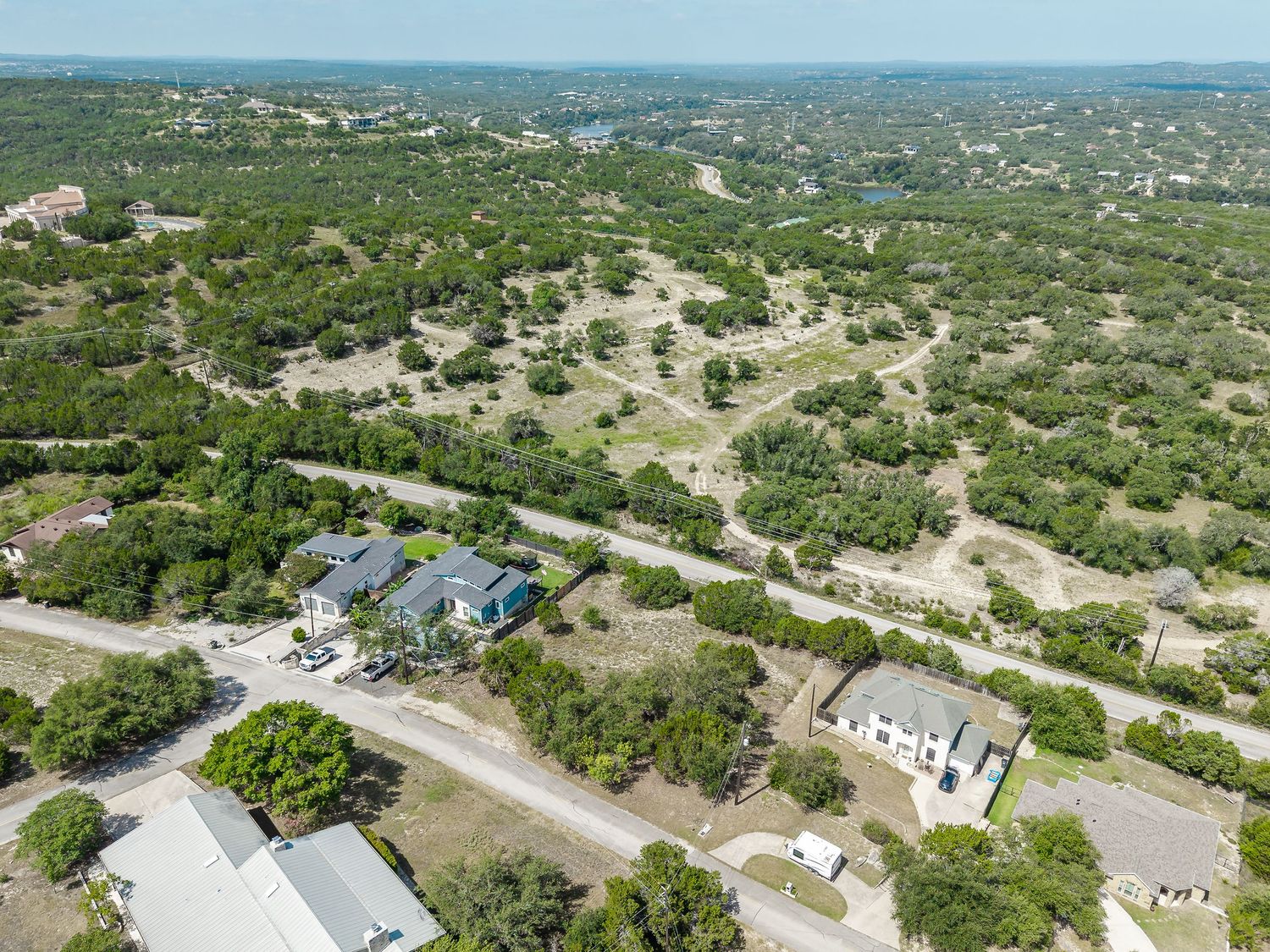 Aerial view of a residential property surrounded by lush Texas Hill Country landscape with winding roads and scattered homes.