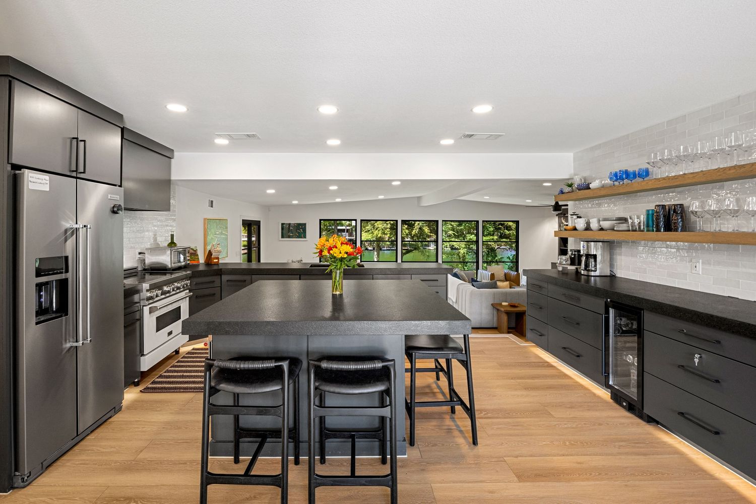 Sleek kitchen with dark cabinetry, large center island, stainless appliances, and open floating wood shelves.