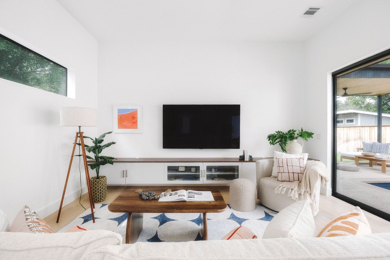 A minimalist white living room features modern furniture, large windows, and natural light creating a bright, airy atmosphere.
