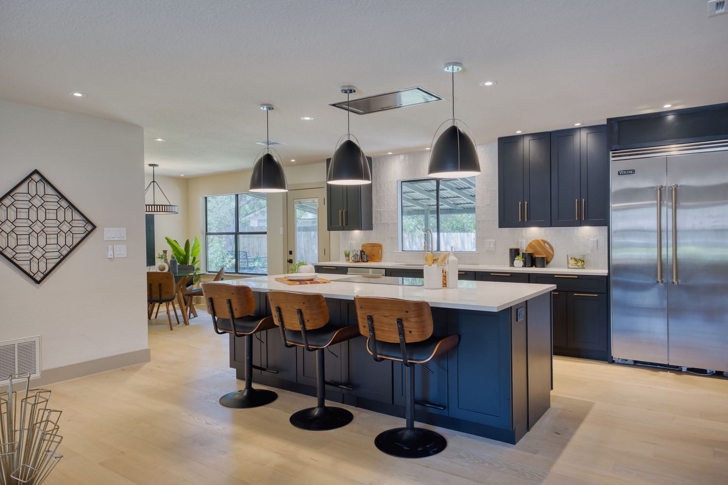 Modern kitchen with navy blue island, bar stools, pendant lights, stainless steel fridge, and white countertops.