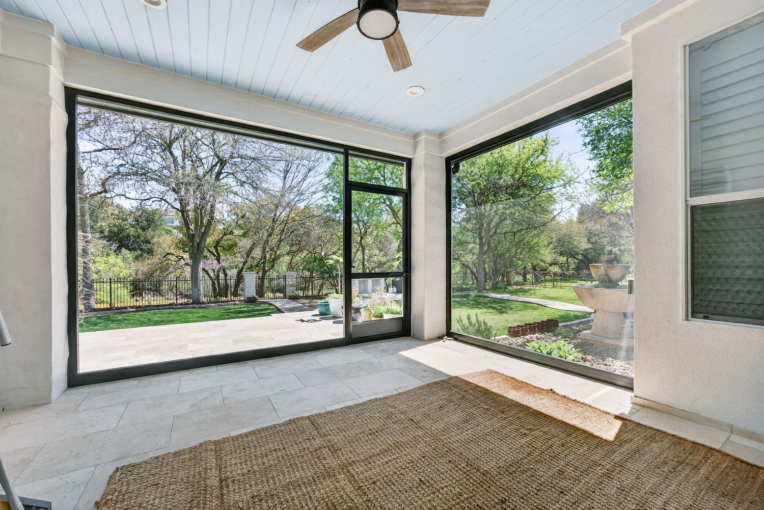 Bright screened porch with floor-to-ceiling windows, ceiling fan, and scenic backyard views through large glass sliding doors.