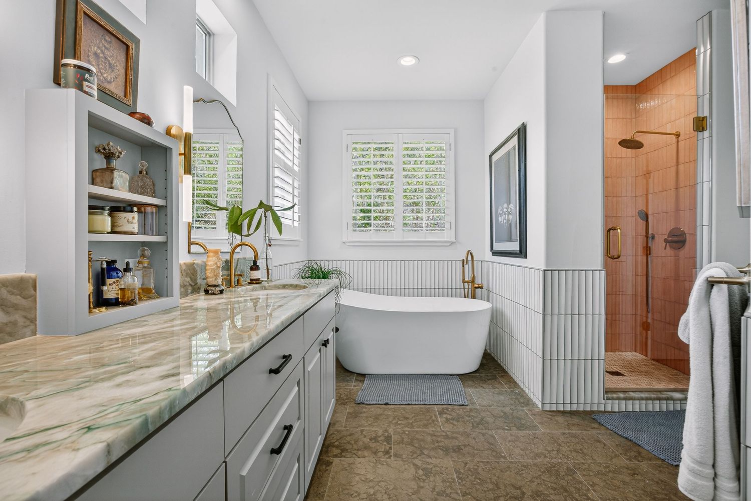 Elegant bathroom with marble countertop vanity, freestanding soaking tub, and glass-enclosed walk-in shower with terracotta tiles.