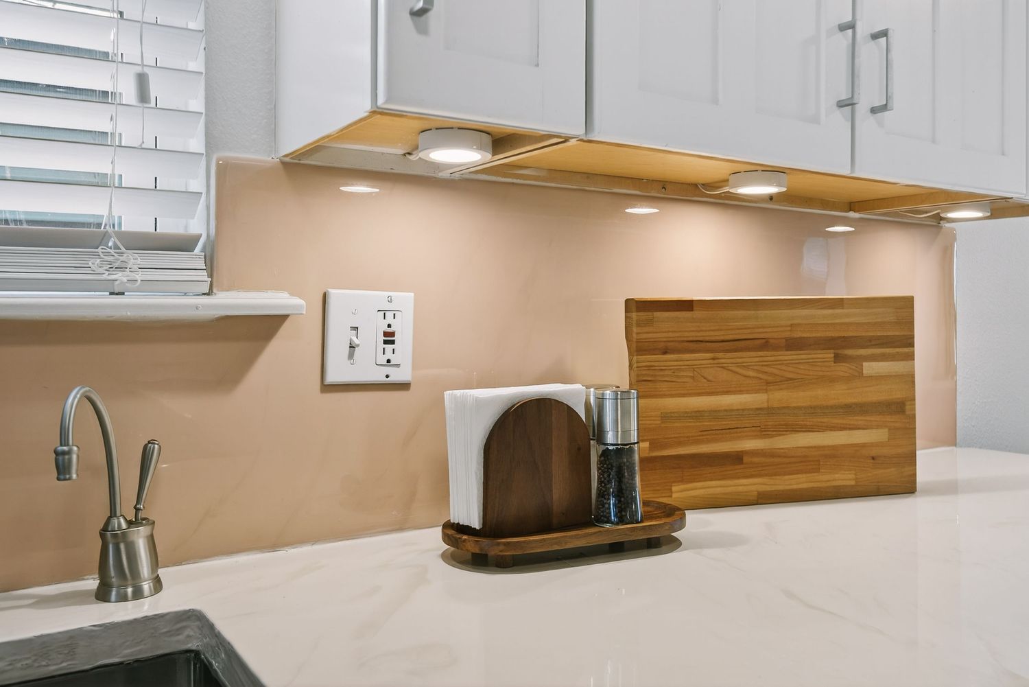 Modern kitchen with white cabinets, wooden backsplash, and under-cabinet lighting showcasing a minimalist design.