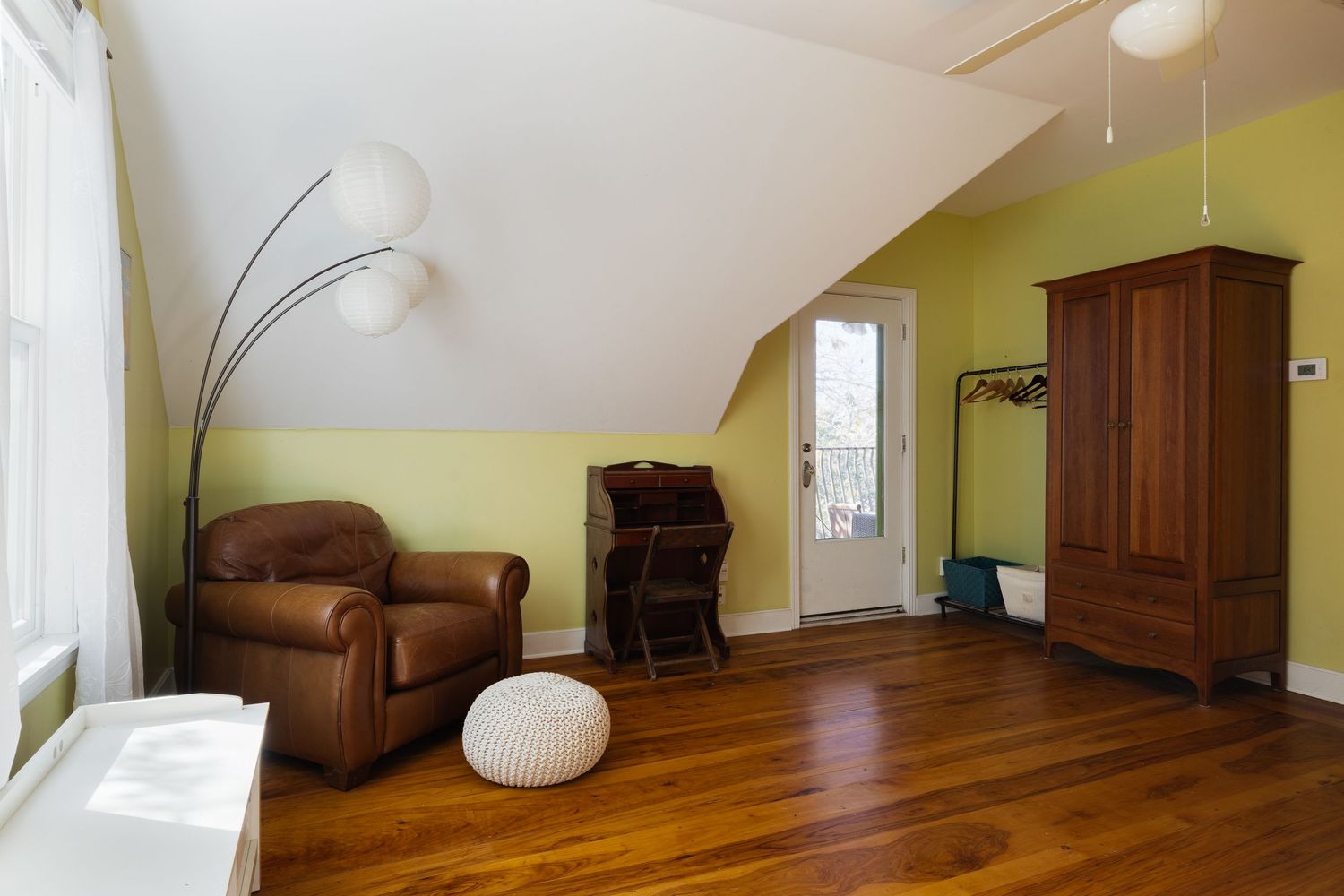 Modern attic bedroom with hardwood floors, brown leather armchair, and lime green accent wall.