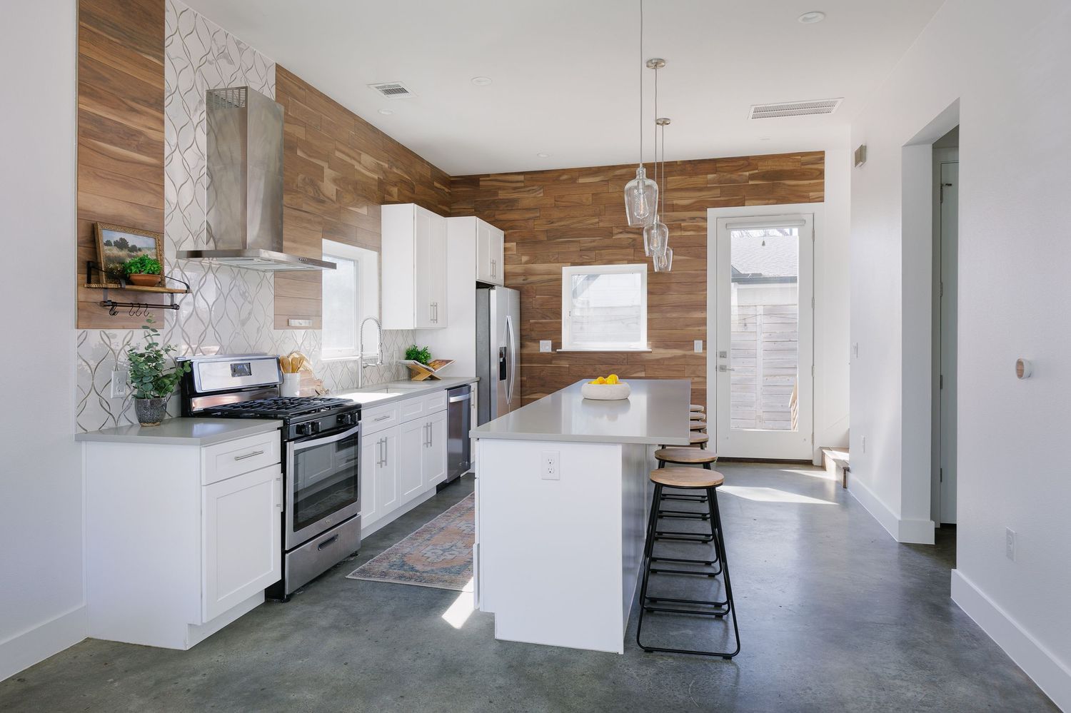 Modern open concept living space with white walls, wood paneling, and natural light streaming through large windows.