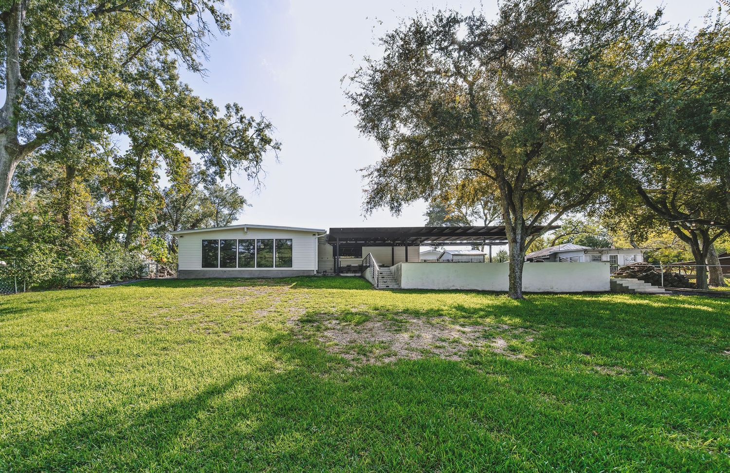 Ranch-style home with large green lawn, mature oak trees, attached carport, and a spacious driveway.