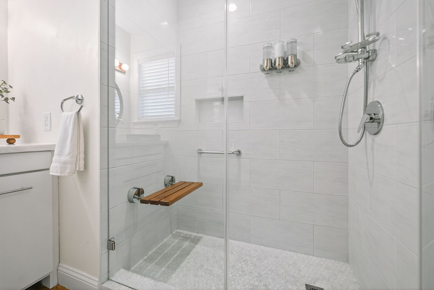 Modern white bathroom interior with glass shower enclosure, subway tile walls, and chrome fixtures.