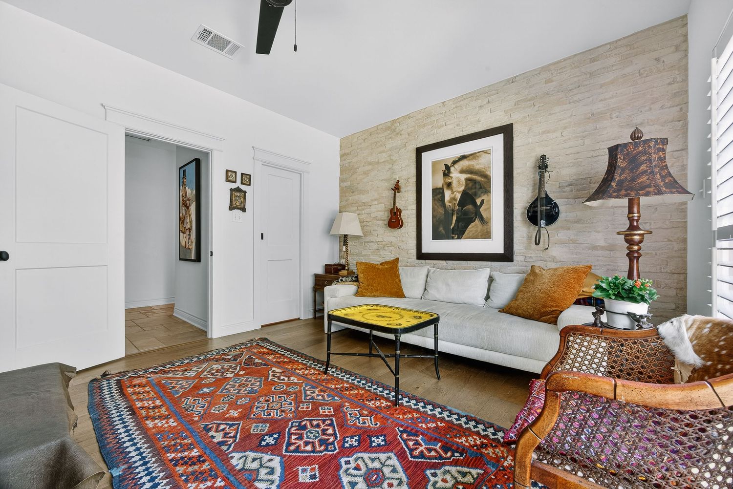 Cozy living room with a colorful kilim rug, white sofa, wooden accent wall, and eclectic decor including artwork and a wicker chair.