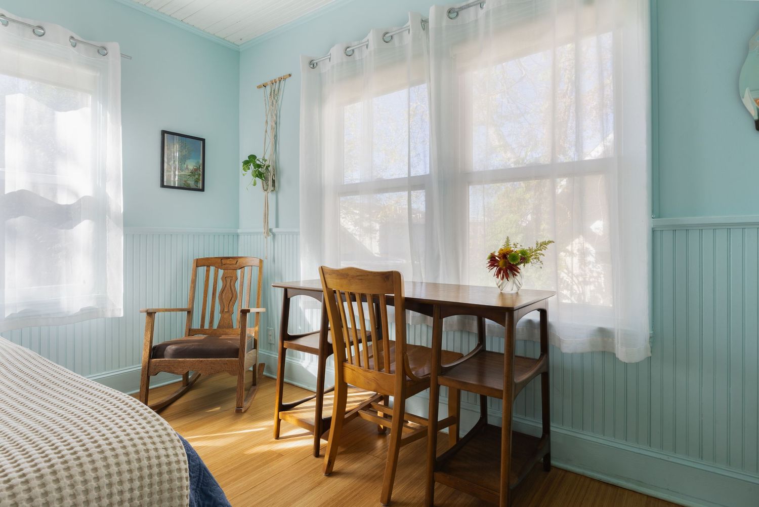 Coastal style bedroom corner with wooden chairs, sheer curtains, and blue wainscoting.