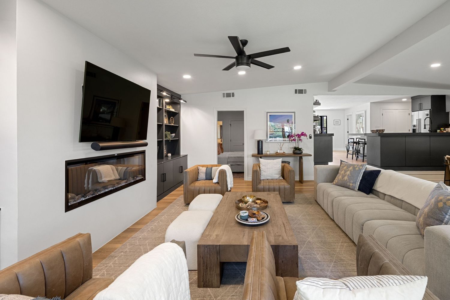 Modern open-concept living room with fireplace, built-in shelves, ceiling fan, and neutral sectional sofa on light hardwood floors.