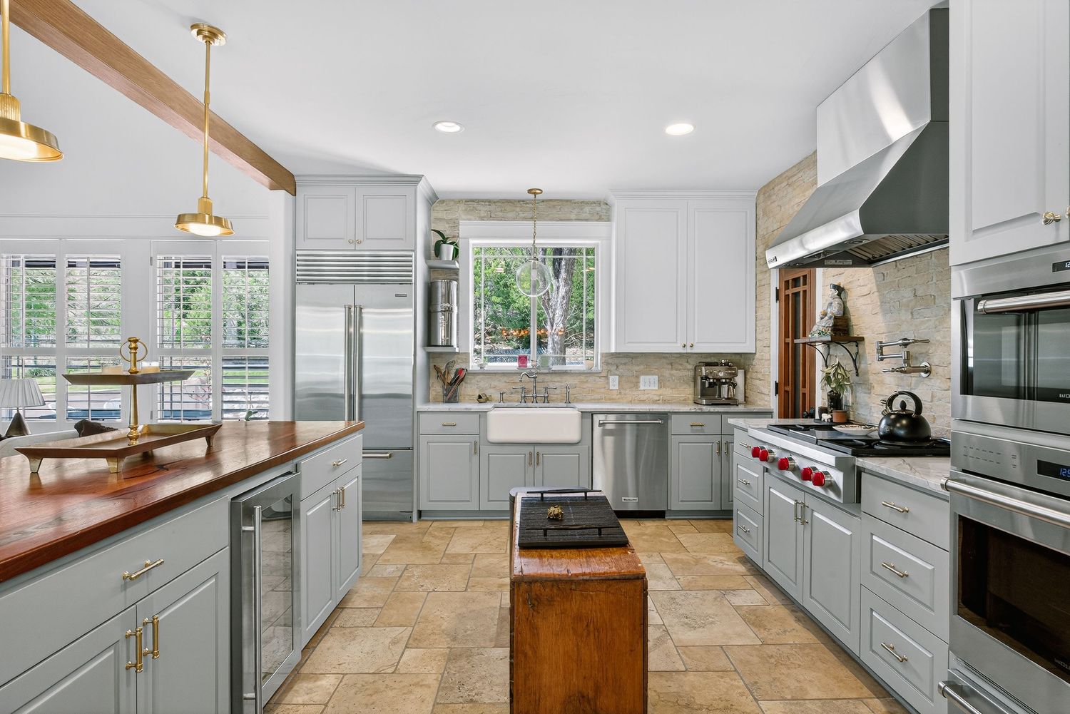 Modern kitchen with gray cabinets, stainless steel appliances, farmhouse sink, wood island, and pendant lights over butcher block counter.