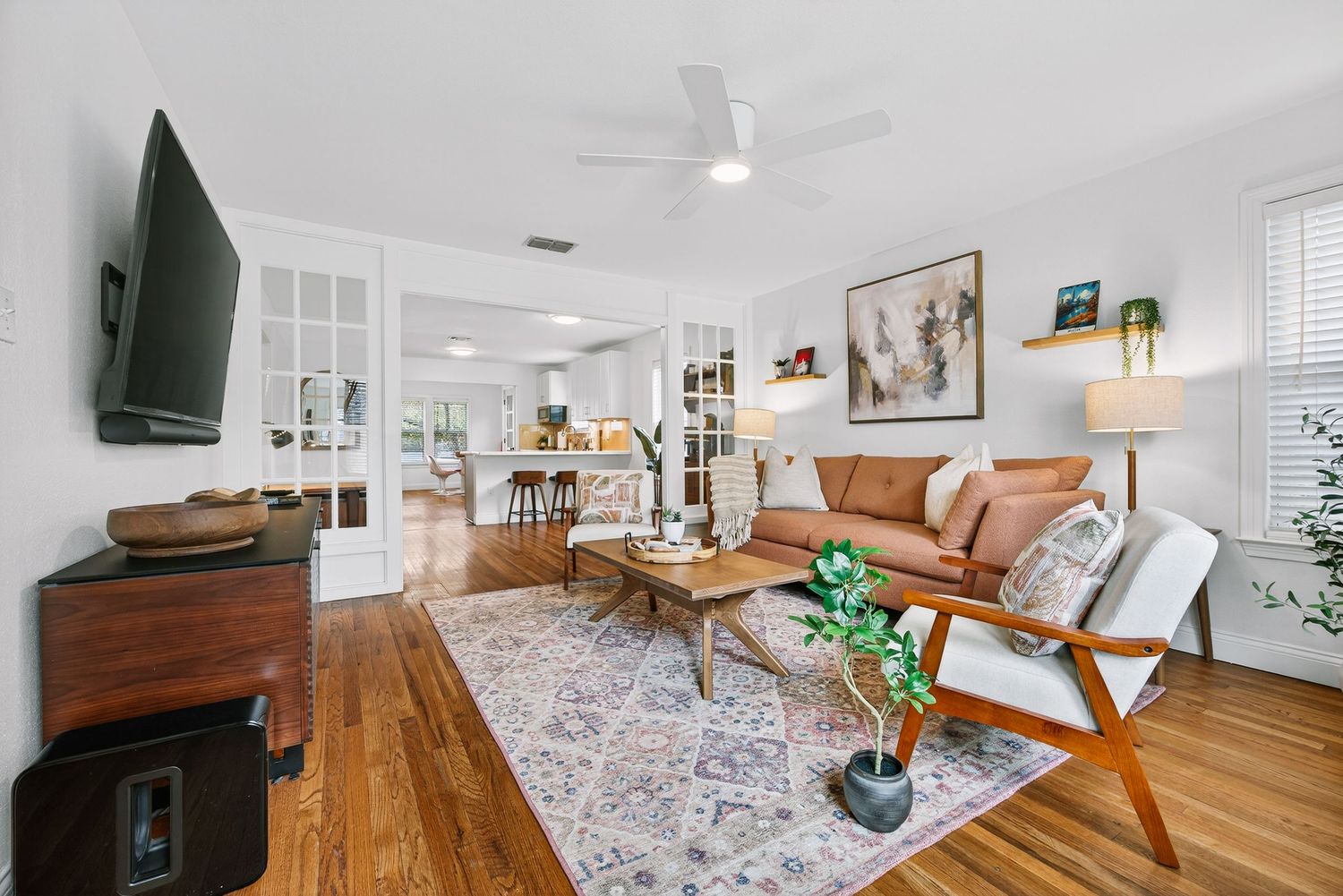 Modern coastal living room features white walls, hardwood floors, and floral area rug with comfortable seating arrangement.