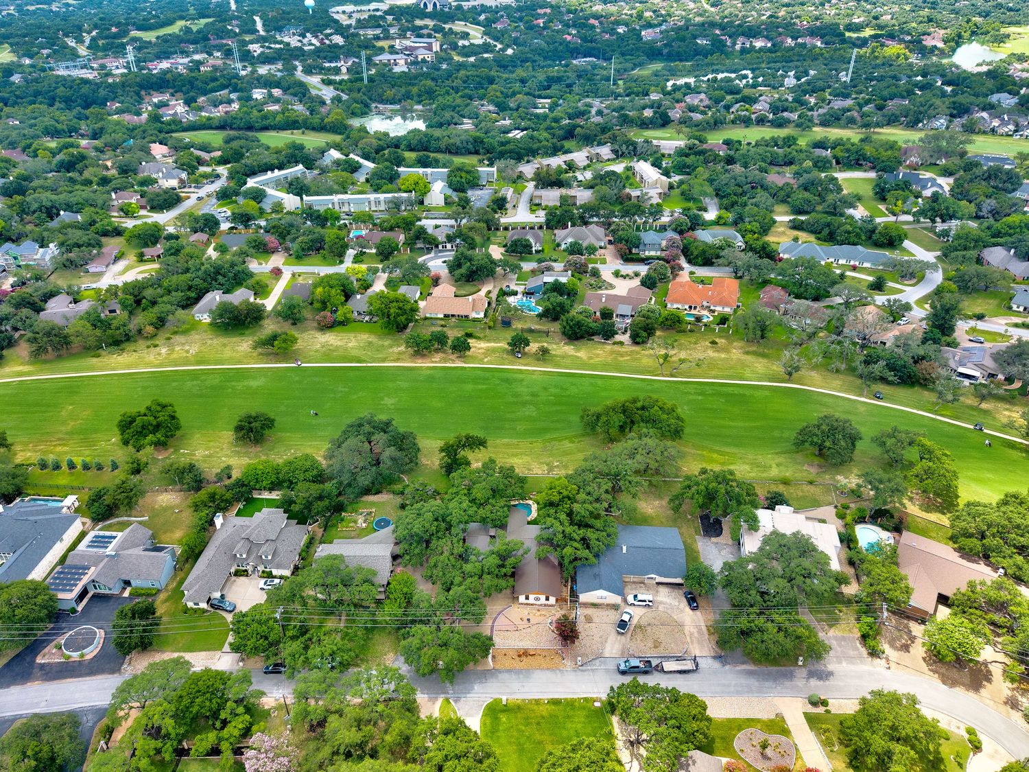 Aerial view of a suburban neighborhood with homes bordering a lush green golf course fairway and surrounded by mature trees.