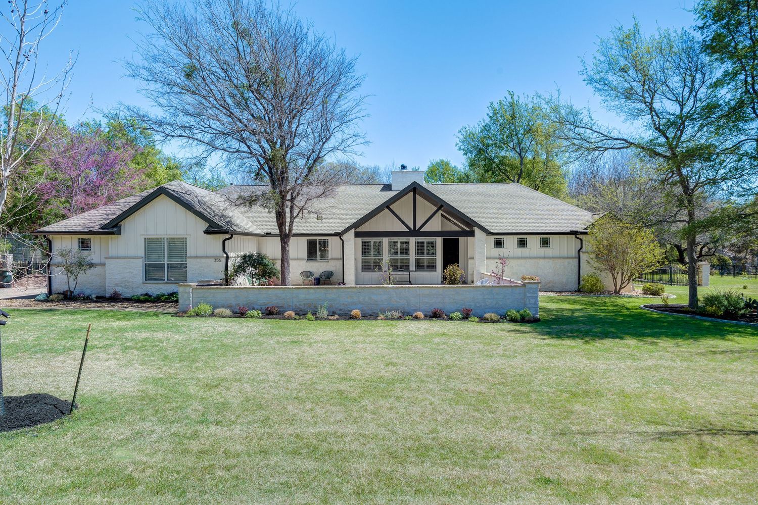 Charming ranch-style home with white exterior, Tudor accents, lush green lawn, and mature trees in spring.