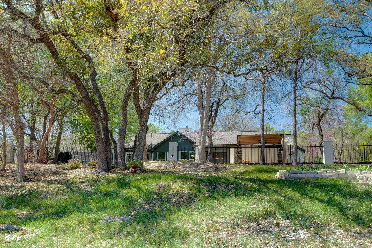 A rustic ranch house nestled among mature oak trees with lush green grass in a serene Texas Hill Country setting.
