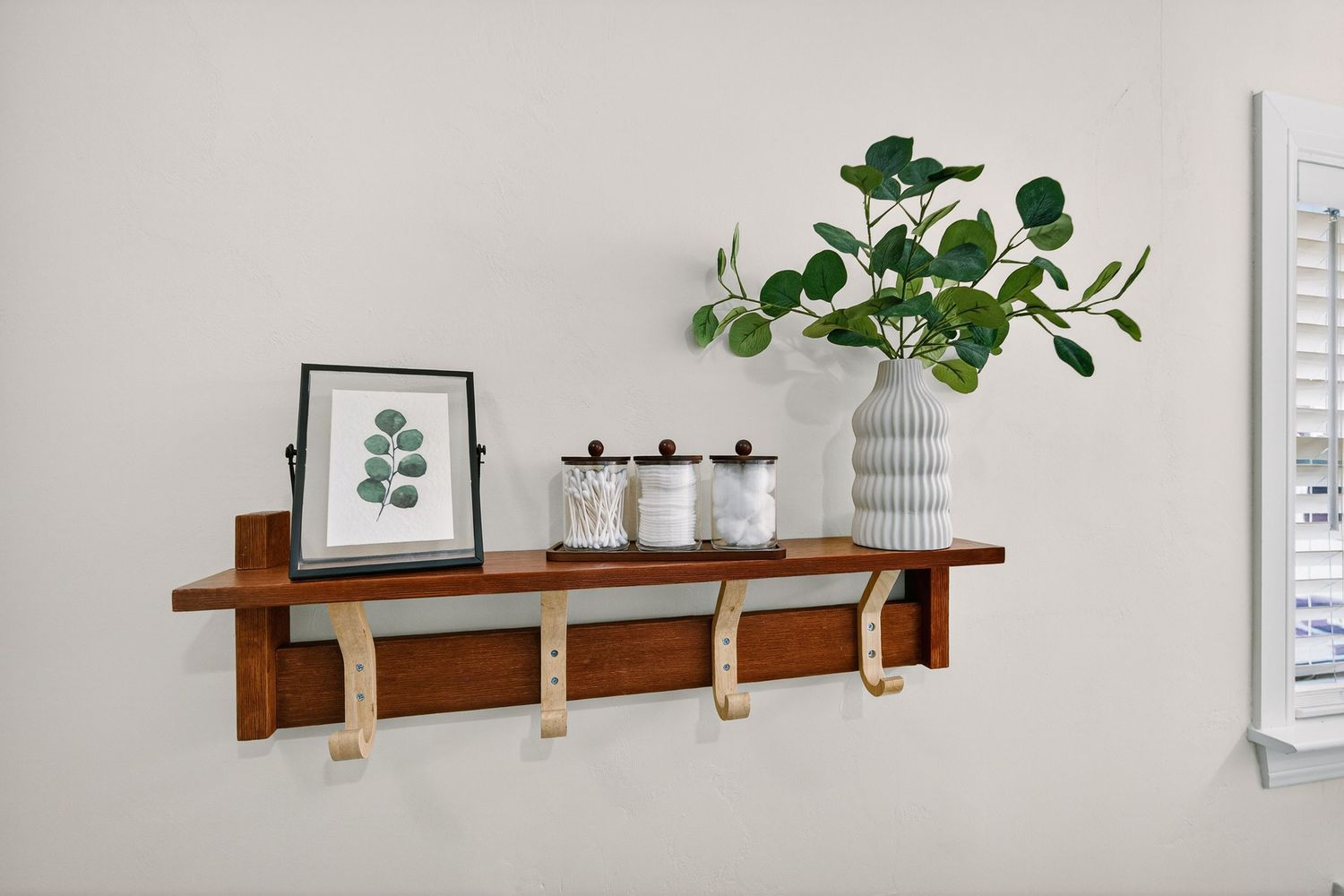 A set of wooden floating shelves mounted on a white wall displaying decorative items and potted plants.