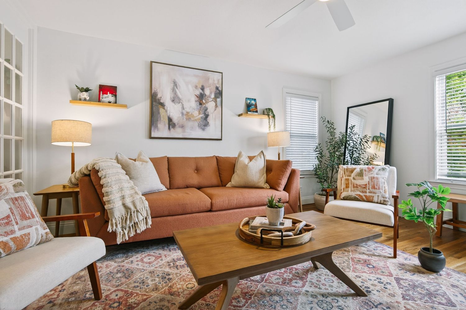 Modern living room with tan leather sofa, white walls, ceiling fan, and decorative artwork displayed on the walls.