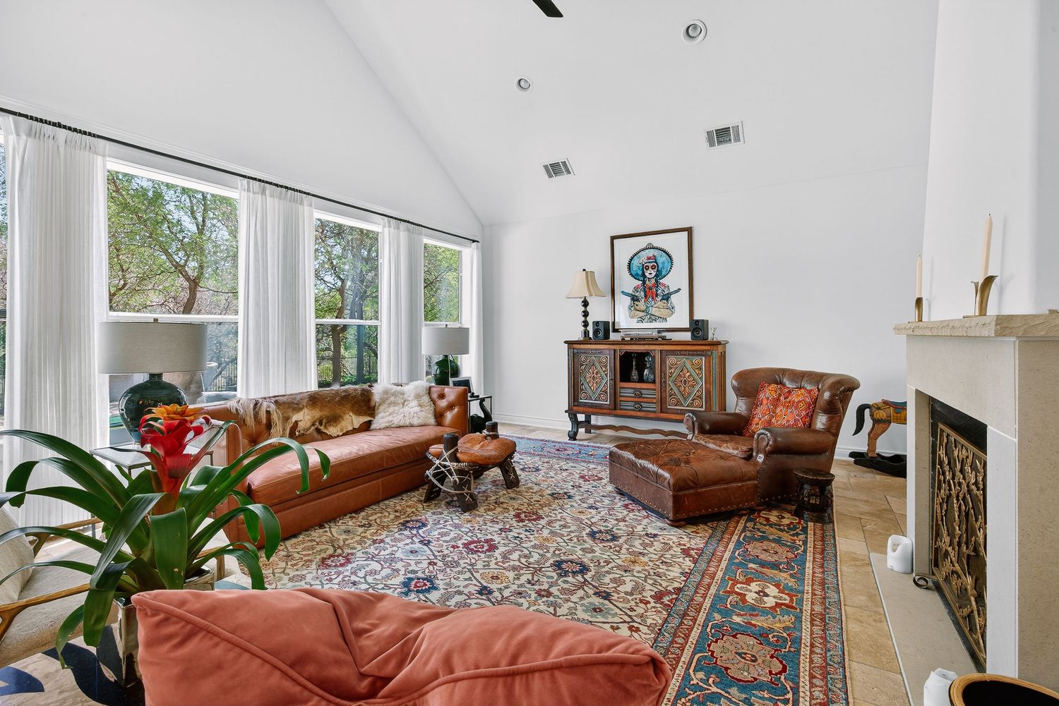 Bright living room with vaulted ceilings, leather sofas, ornate area rug, fireplace, and large windows with natural light.