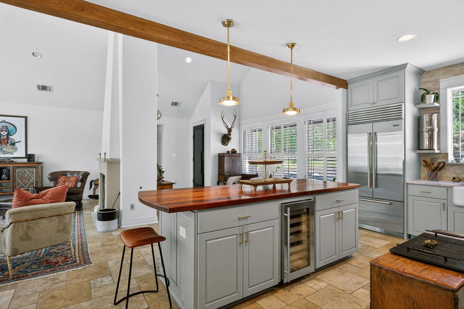 Gray kitchen island with wood countertop, wine fridge, pendant lights, and built-in cabinets in an open-concept home.