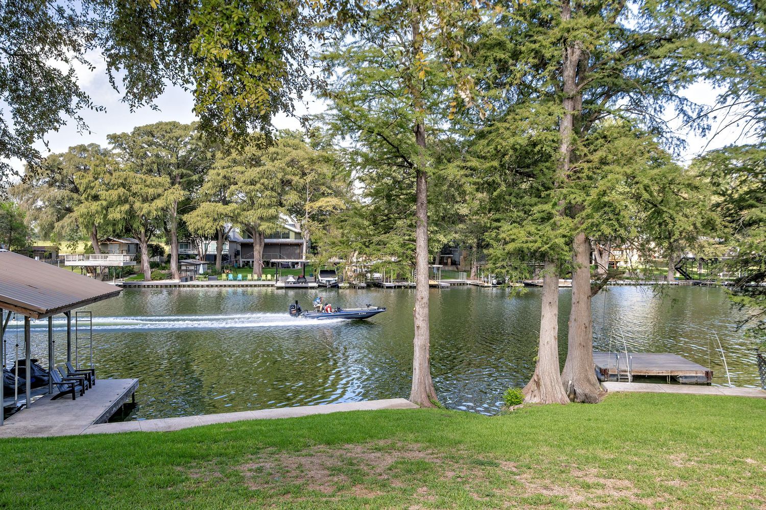 Serene lakefront property with mature cypress trees, green lawn, private dock, and calm water views.