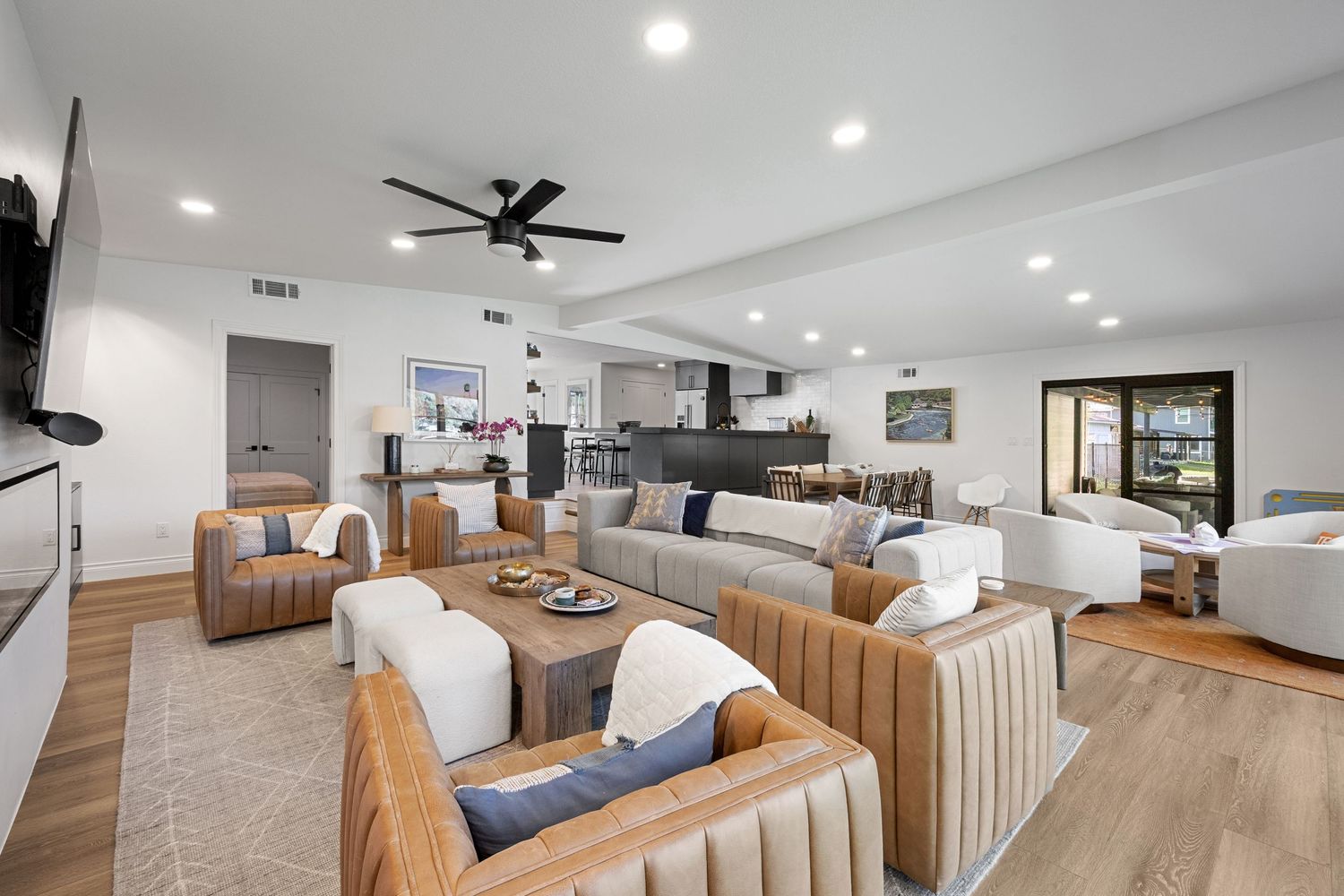 Modern open-plan living area with rattan chairs, neutral tones, ceiling fan, and seamless flow to kitchen.