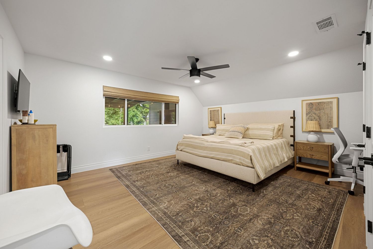 Spacious master bedroom with light wood floors, ceiling fan, neutral tones, and large area rug.