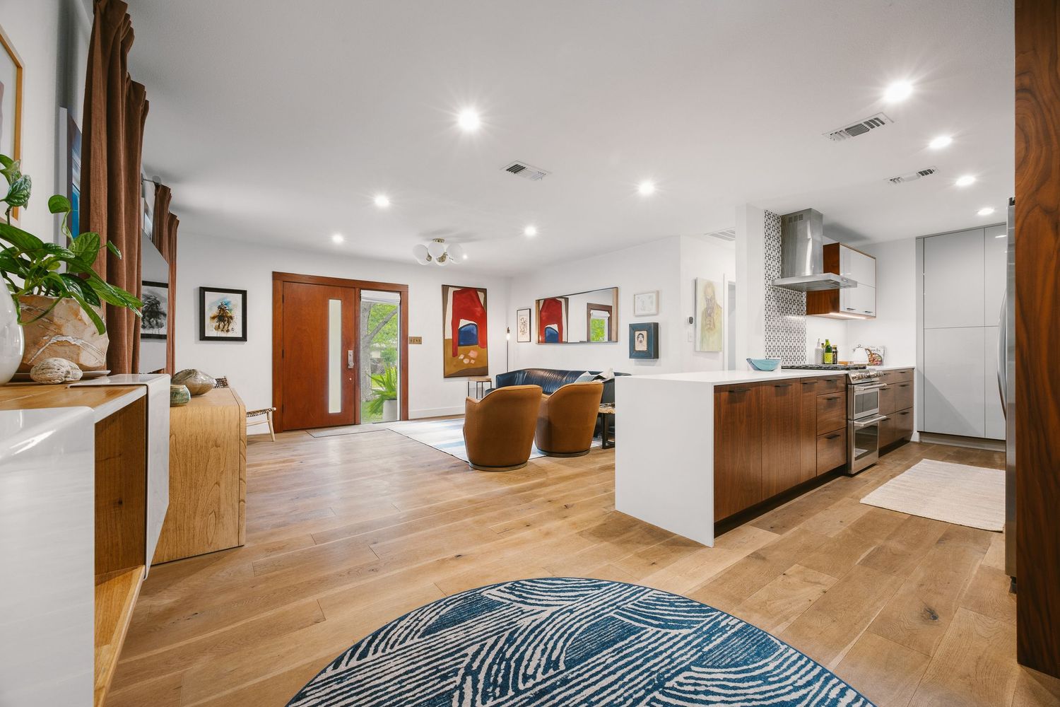 Open-concept living space with hardwood floors, modern kitchen island, recessed lighting, and a vibrant blue area rug.