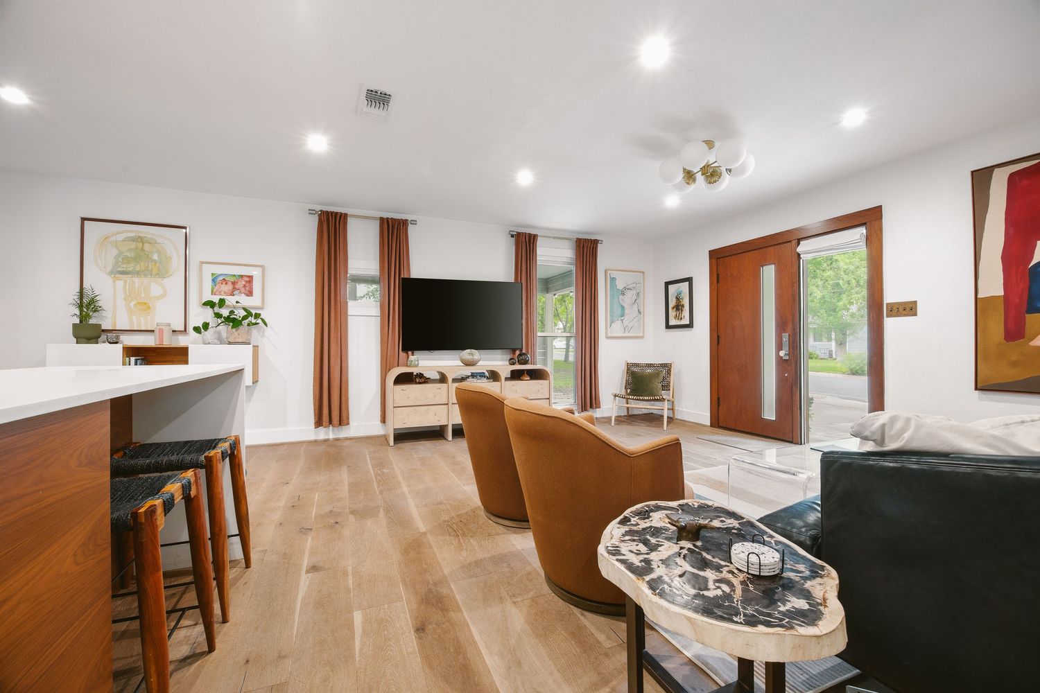 Modern open-concept living room with light hardwood floors, leather chairs, wall-mounted TV, and bar seating area.