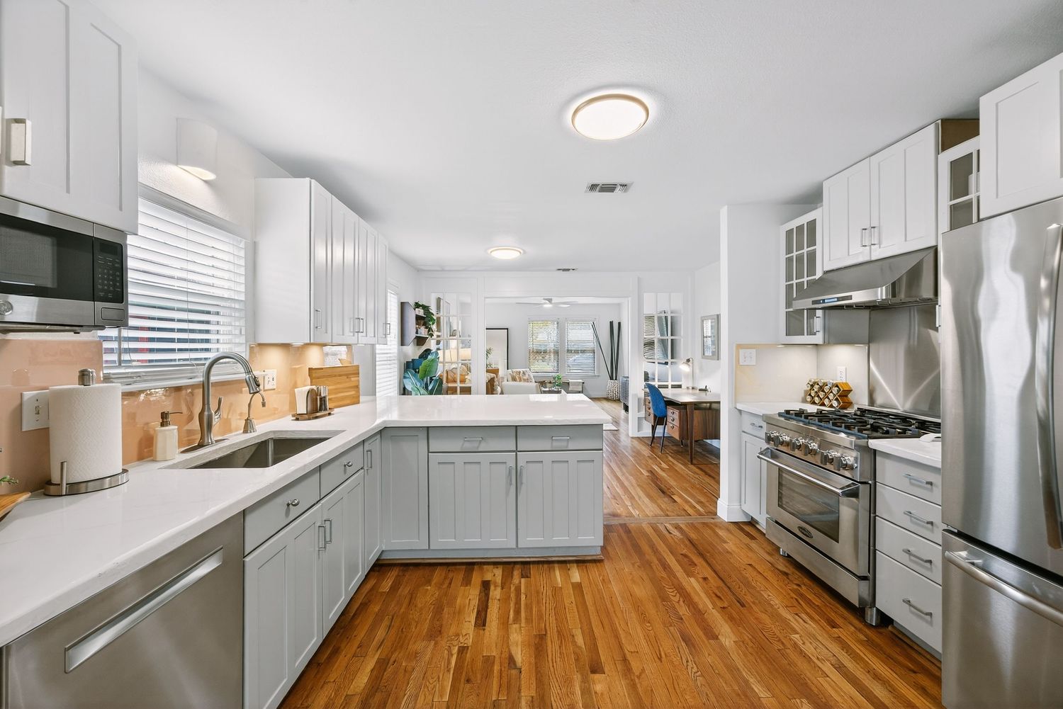 Bright galley kitchen featuring gray cabinets, stainless appliances, and warm wood flooring.