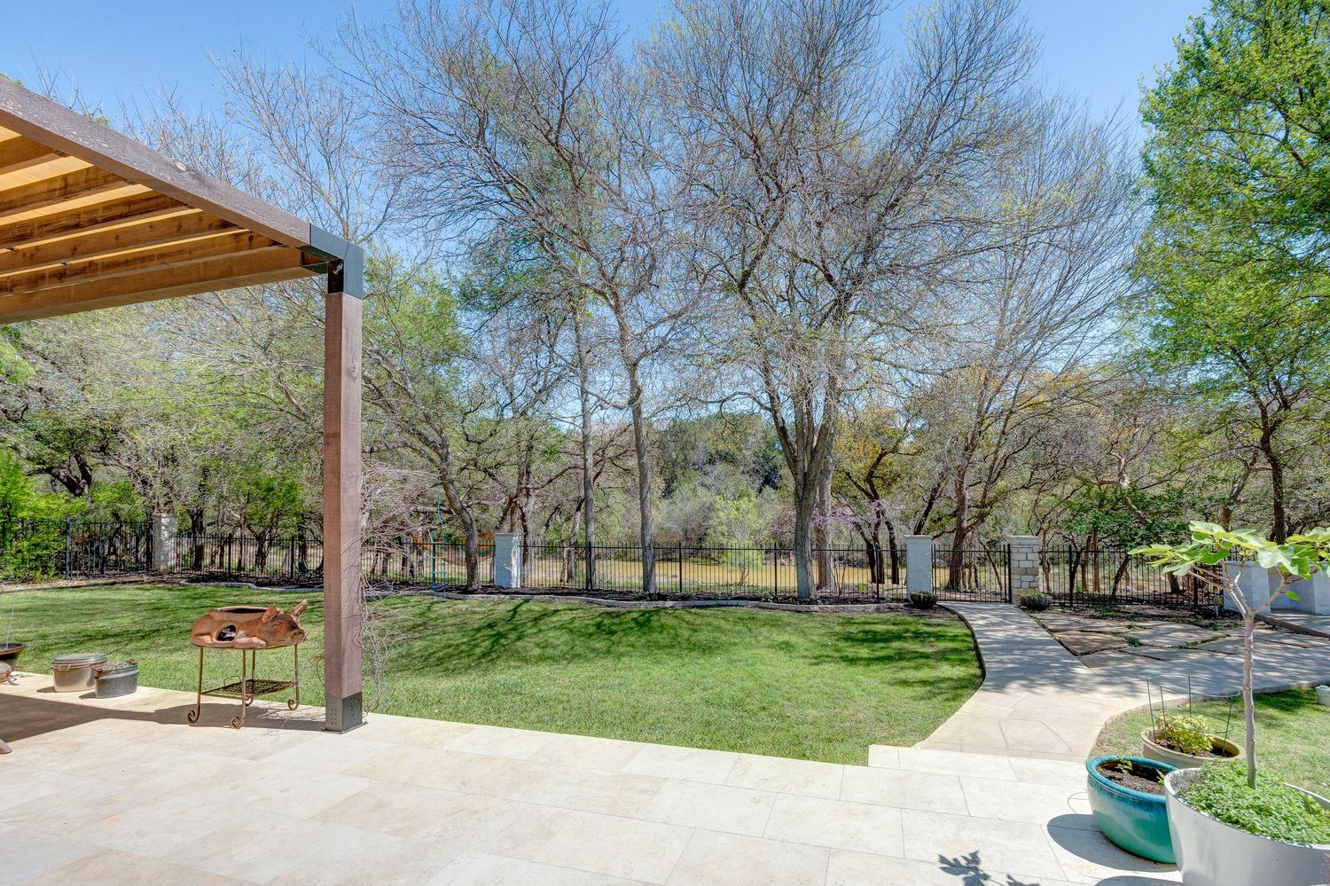 Spacious backyard patio with lush green lawn, mature trees, and serene water view on a sunny day.
