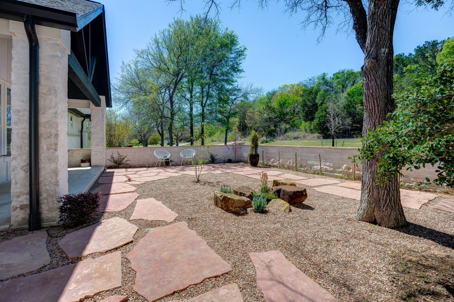 Landscaped backyard with flagstone path, gravel garden, wooden benches, and mature trees near a white fence.