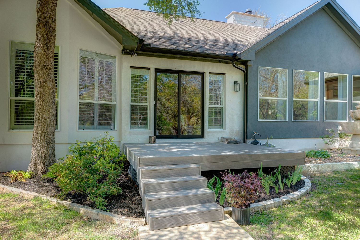 Ranch-style home exterior featuring concrete steps, manicured landscaping, large windows, and a charming back patio entrance.