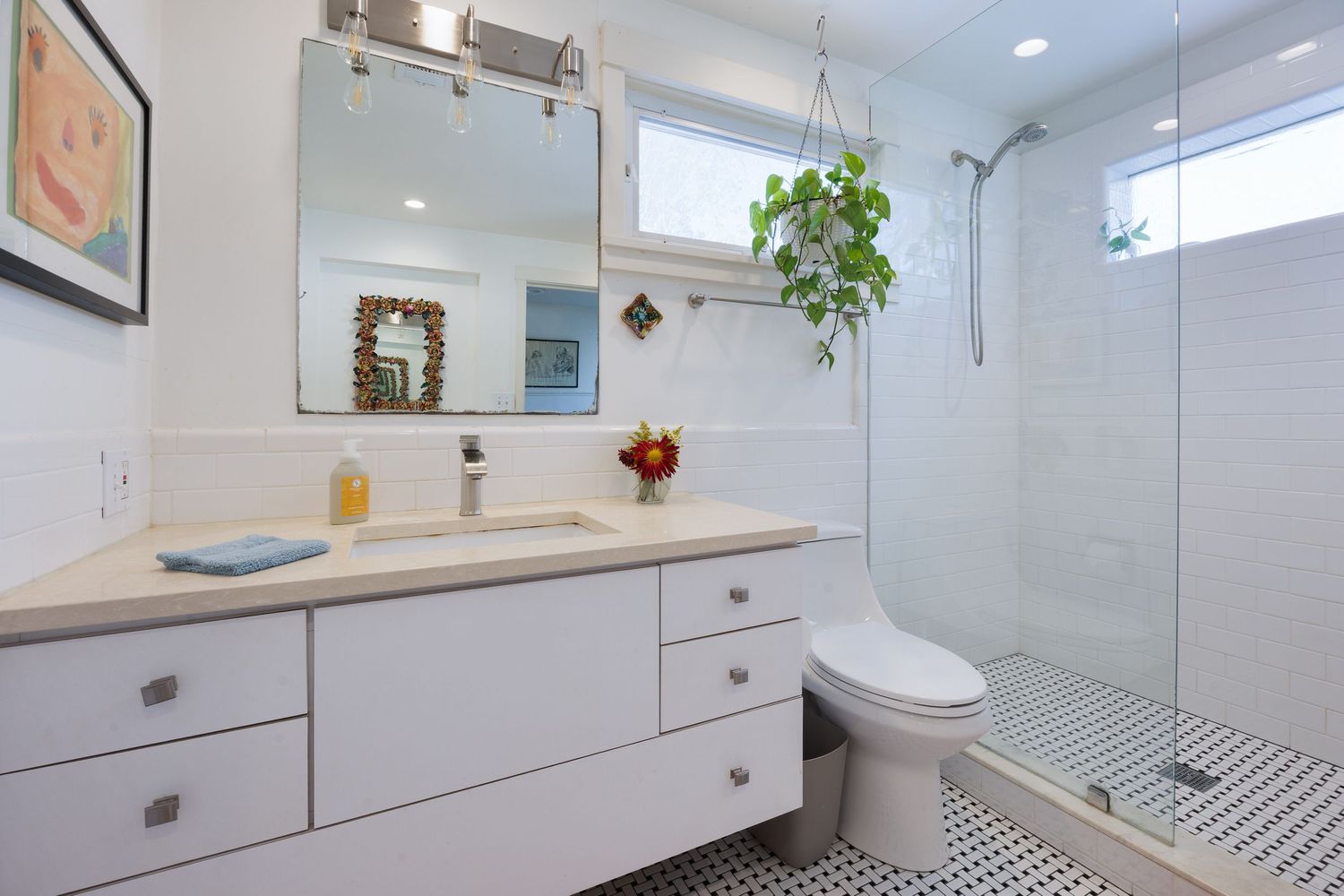 Clean white bathroom with glass shower, floating vanity, and decorative plants.