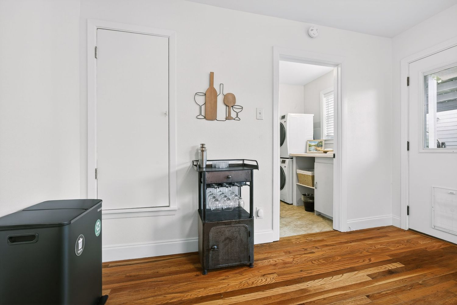 Empty room with hardwood floors, white walls, and a small black heater near a doorway leading to another space.