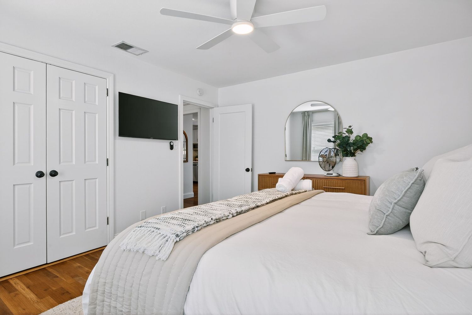 Modern white bedroom with ceiling fan, wooden flooring, and minimalist decor featuring a clean, bright aesthetic.