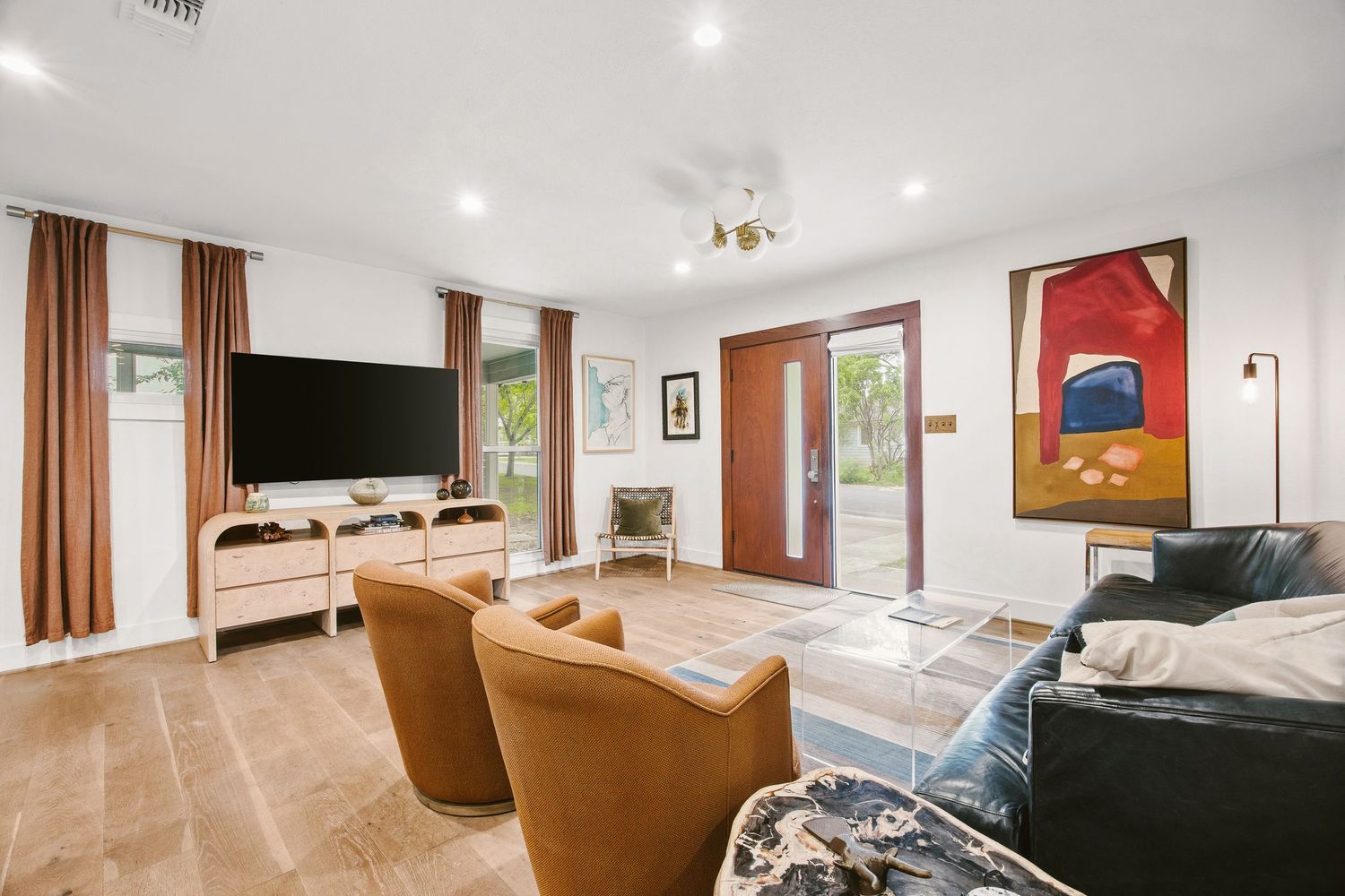 Bright living room with tile floors, leather sofa, orange chairs, wall-mounted TV, and glass doors leading to a patio.