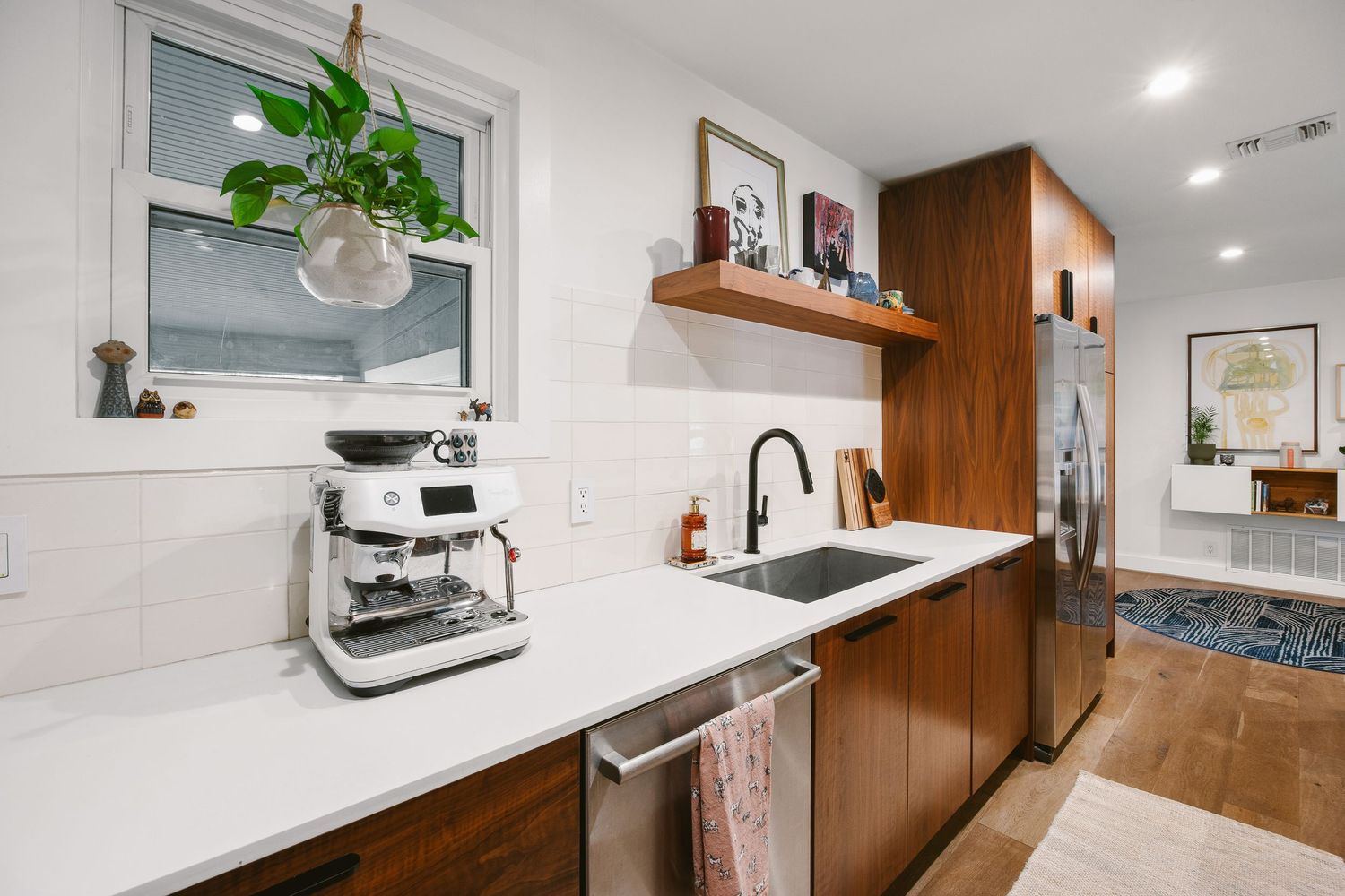 Modern kitchen with walnut cabinets, white quartz countertops, black sink faucet, espresso machine, and stainless steel refrigerator.