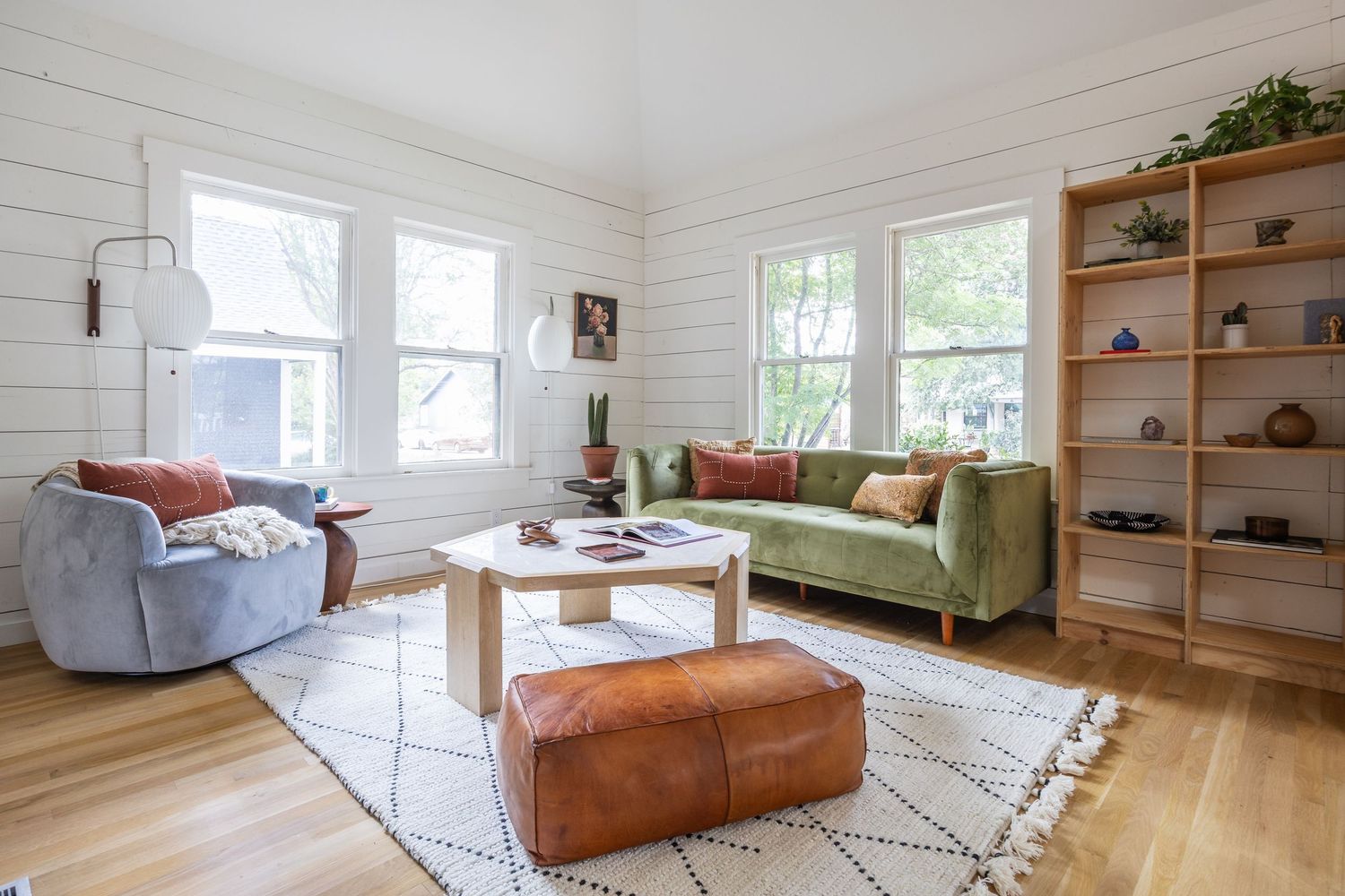 Bright white living room with hardwood floors, leather furniture, and built-in wooden shelving.