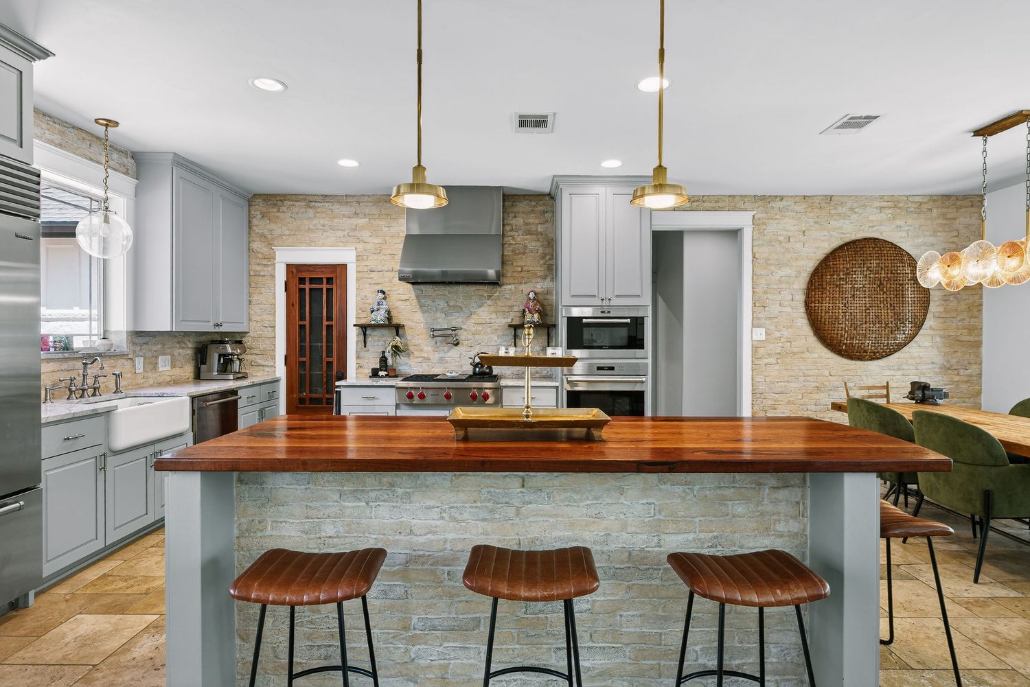 Modern kitchen with gray cabinets, wood butcher block island, pendant lights, brick backsplash, and industrial bar stools.