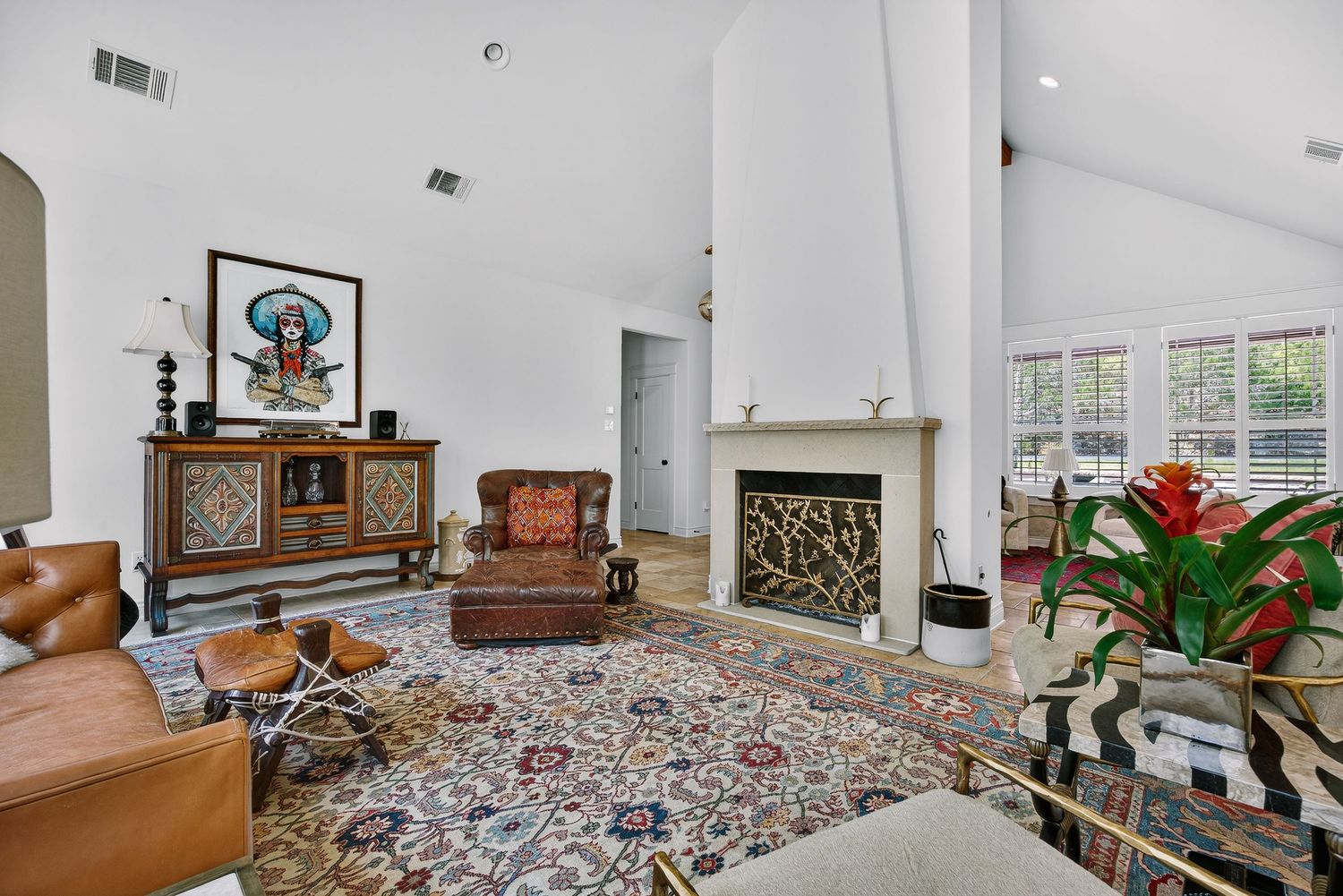 Bright living room with vaulted ceilings, decorative fireplace, leather furniture, and colorful Persian rug on light tile floors.