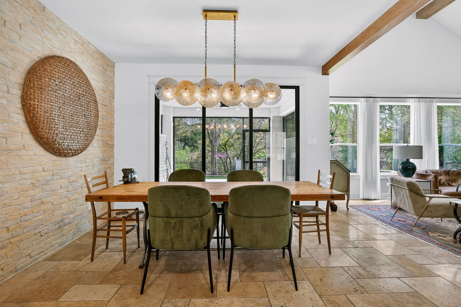 Elegant dining room with green velvet chairs, wood table, globe chandelier, exposed beams, and stone accent wall.