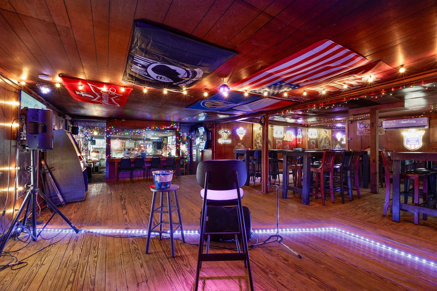 Colorful bar interior with LED lights, bar stools, hardwood floors, and festive string lights on the ceiling.