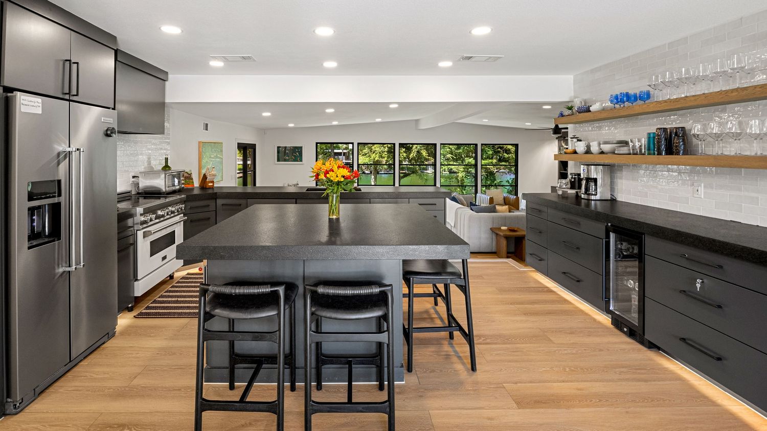 Gourmet kitchen with stainless steel appliances, dark island, open wood shelving, and light hardwood floors.