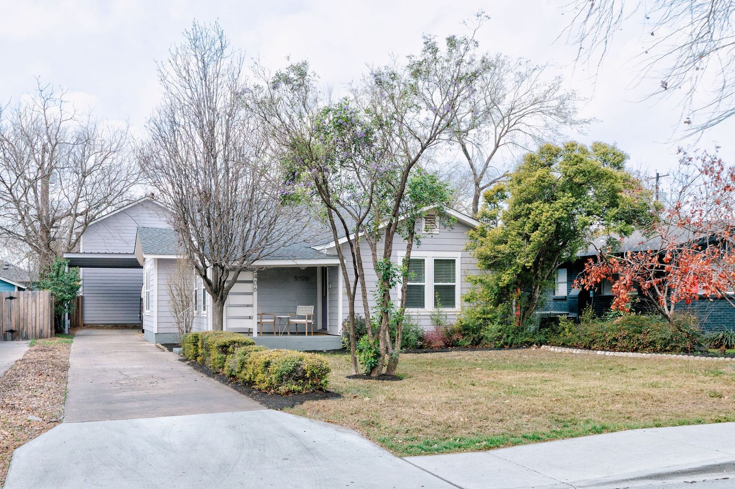 A curved residential driveway leads up to a house with landscaped yard and trees on a cloudy winter day.