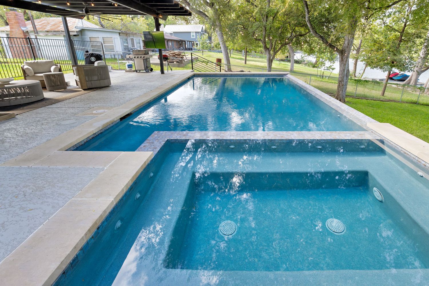 Luxurious outdoor pool and spa with water features, surrounded by manicured lawn and mature shade trees.