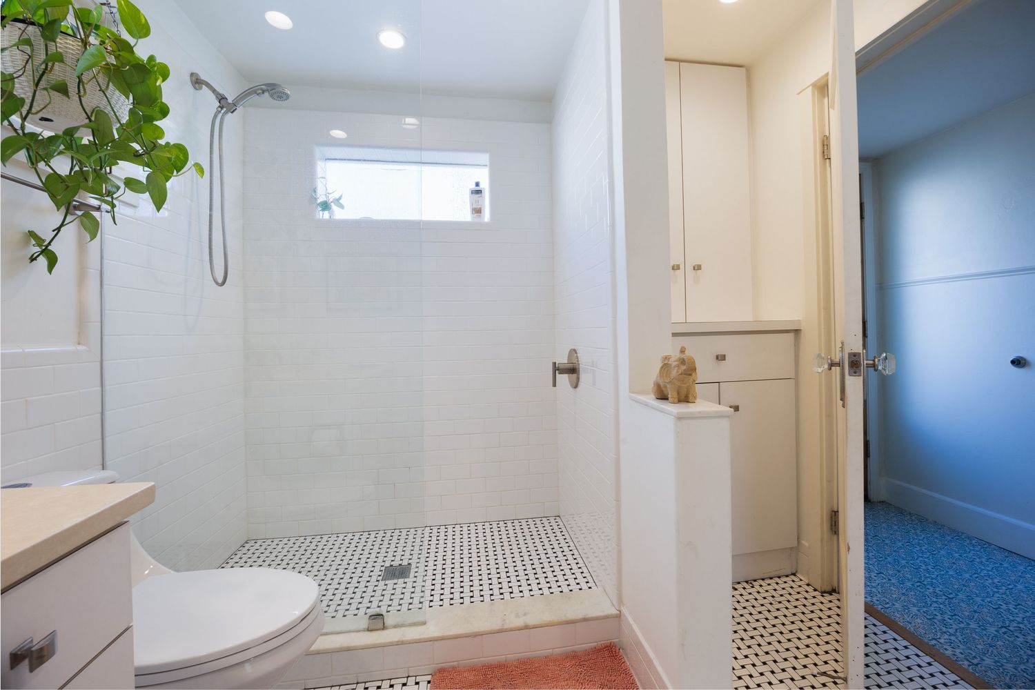 Bright bathroom with white tile shower, floating vanity, and black and white floor pattern.